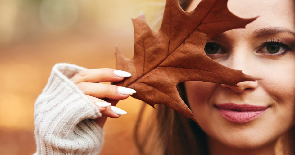 Jesienna sceneria. Kobieta zasłaniająca jedno oko brązowym liściem.